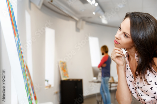 Young caucasian woman standing in art gallery front of  paintings
