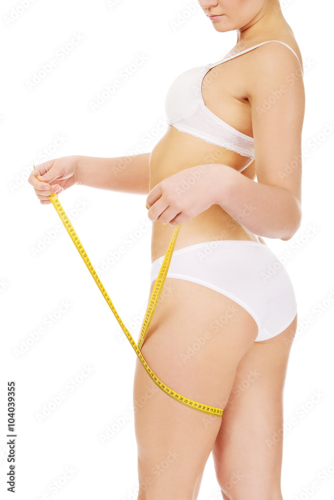 Naklejka premium Young slim woman measuring her thigh with a yellow tape 
