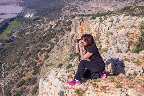 woman in a black tracksuit photographing sitting on the edge of the cliff photo