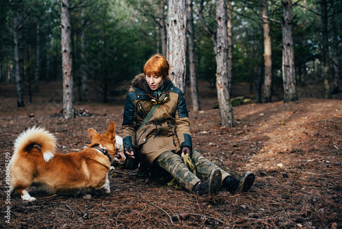 redhead girl walking with welsh corgi dog in the forest