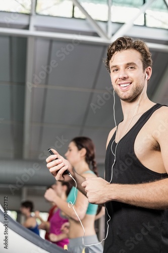 Smiling muscular man on treadmill listening to music