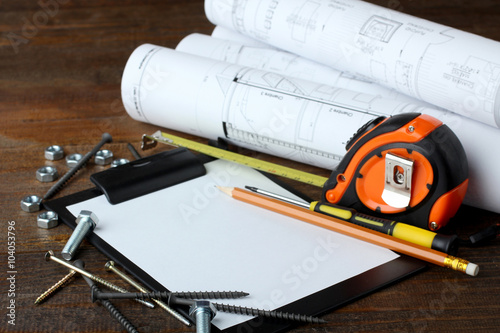 screws of different shapes and roulette with drawings and many other tools on the wooden brown table photo