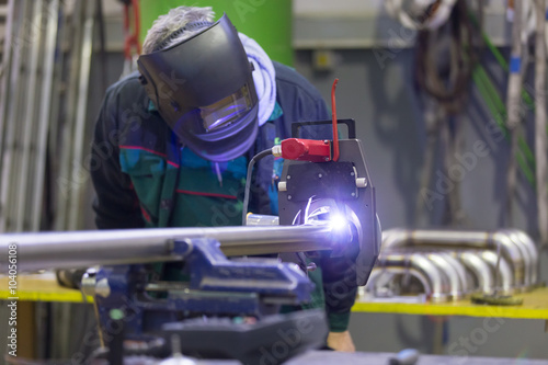 Industrial operator setting  computer controlled process of orbital welding machine in inox pipes manufacturing workshop.