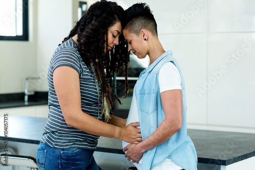 Pregnant lesbian couple embracing in kitchen