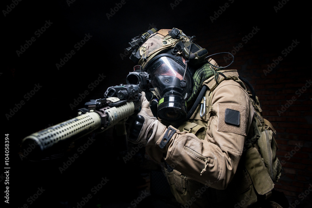 Soldier in gas mask aiming from his rifle.Selective focus/Man in uniform,helmet and gas mask aiming from assault rifle on  dark background
