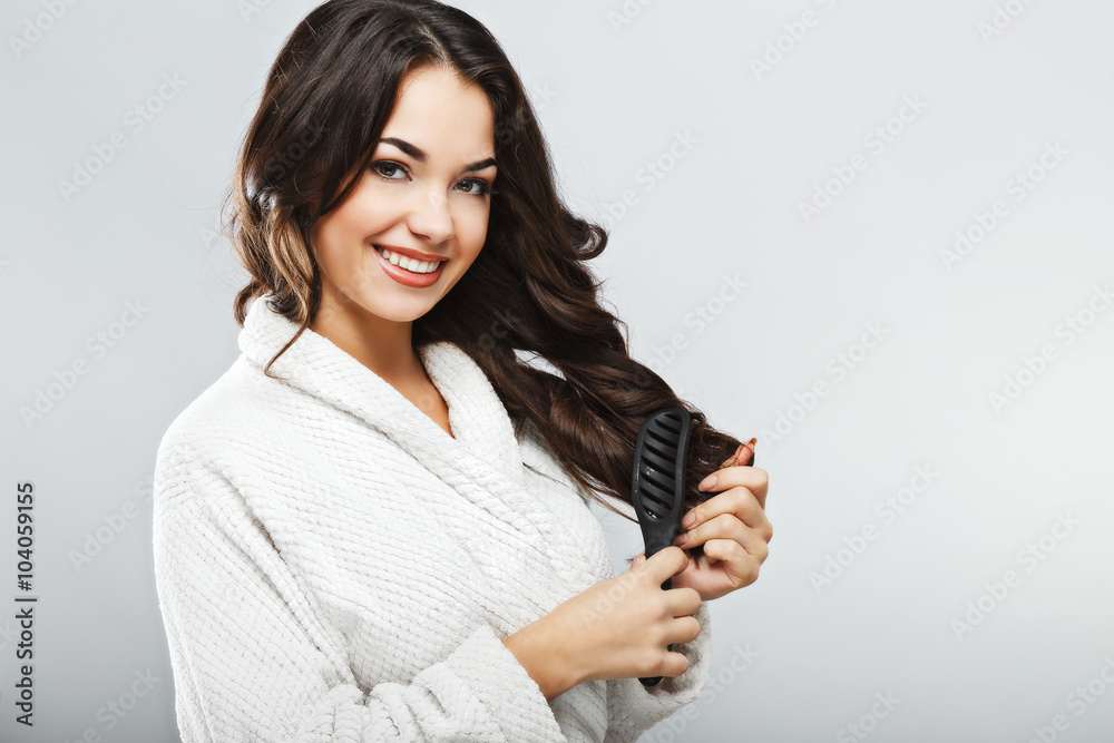 Pretty girl wearing bath robe brushing hair at white studio background Pretty girl wearing bath robe brushing hair at white studio background