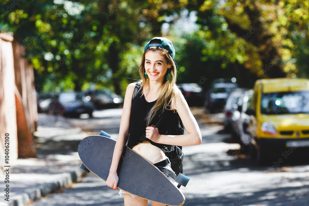 Attractive blond girl posing with black skateboard on the street