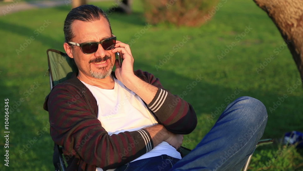 Middle age man sitting on a park bench and talking on the smart phone Middle age man sitting on a park bench and talking on the smart phone