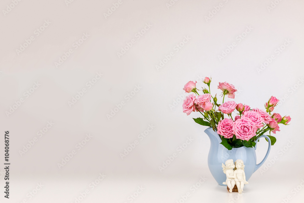 Pink flowers in blue jug. Roses in jug. Two angels on wooden banch.