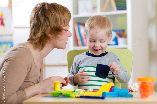 Little boy is learning to use colorful play dough with mother help