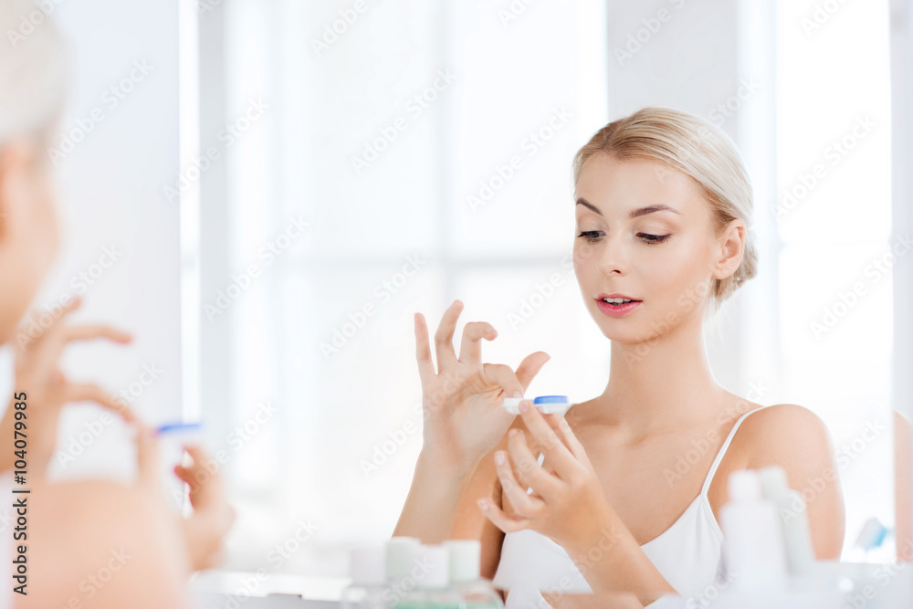 young woman putting on contact lenses at bathroom