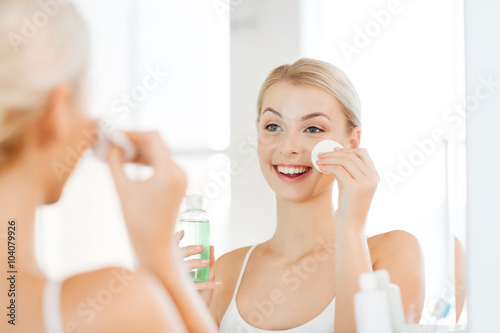 young woman with lotion washing face at bathroom