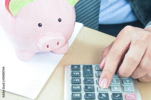 business man using calculator and piggy bank on office desk