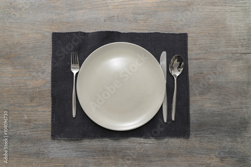 An off-white plate with fork, knife and spoon on a black placemat on a wooden table photo