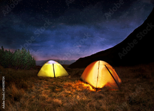 Illuminated yellow camping tent under stars at night