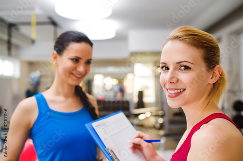 Woman in gym, personal trainer, consultiing plan on clipboard