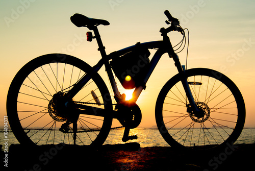 Silhouette of mountain bike at sea with sunset sky background