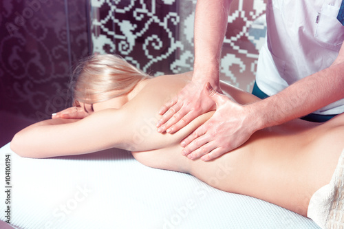 Man makes a back massage for a young blonde woman