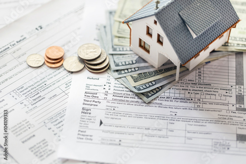 Miniature house with money on tax papers