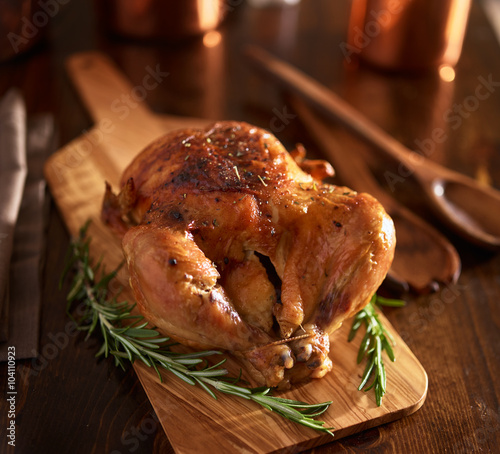 rotisserie chicken on wooden serving tray with herbs and rosemary photo