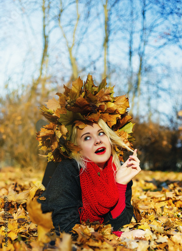 High fashion blonde girl with the red lips in the wreath of leaves and in the fallen leaves in the park outdoor