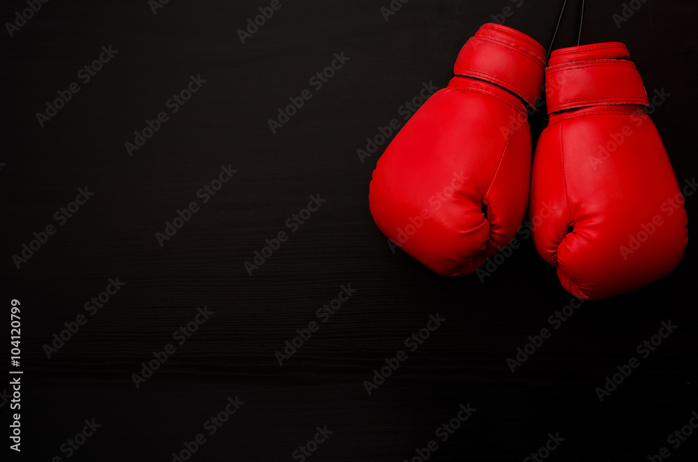 Two red boxing gloves in the upper corner of the frame over a black background, empty space