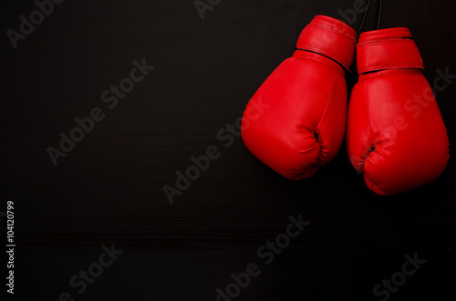 Two red boxing gloves in the upper corner of the frame over a black background, empty space © somemeans