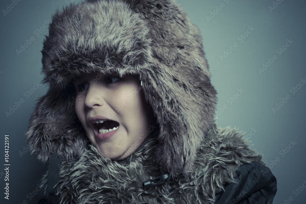 Funny child with fur hat and winter coat, cold concept and storm Funny child with fur hat and winter coat, cold concept and storm