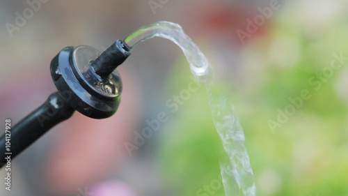 Closeup of a watering system dripper (emitter) suspended in mid-air, dripping water. Very shallow focus on emitter. photo