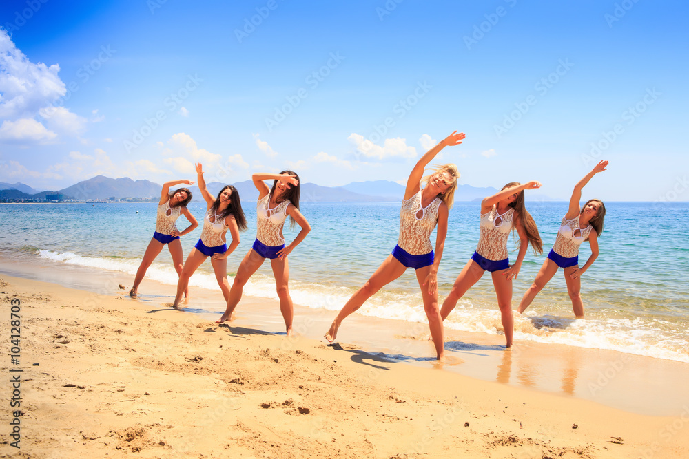 cheerleaders stand in triangle hands over head on wet sand