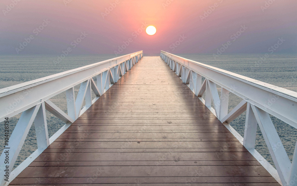 The bridge leads to the sea during sunset.