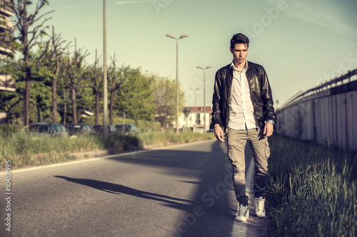 Young man in black leather jacket walking along