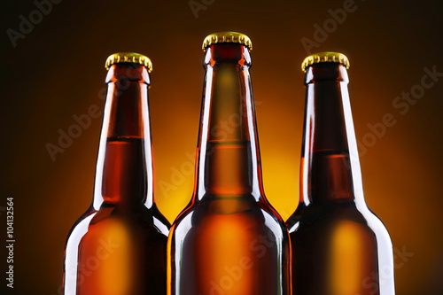 Three brown glass bottles of beer on dark lighted background  close up