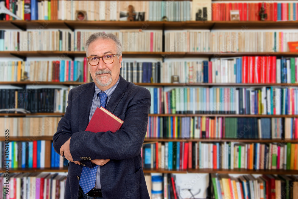 Senior teacher standing holding a book in front of a bookcase Senior teacher standing holding a book in front of a bookcase