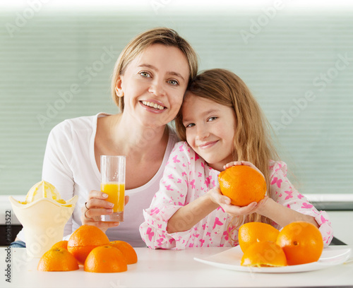 Mother and daughter make orange juice on a juicer