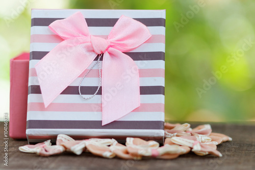 Present / Gift surrounded with small bows on wooden table with green beautiful Bokeh in the background
