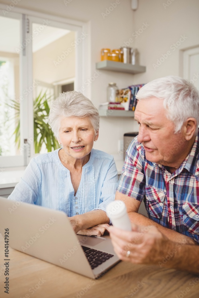 Senior couple holding a pill bottle while operating laptop Senior couple holding a pill bottle while operating laptop