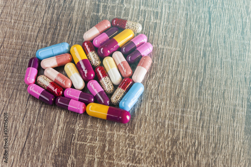 Medicine capsules forming a heart on a wooden surface photo