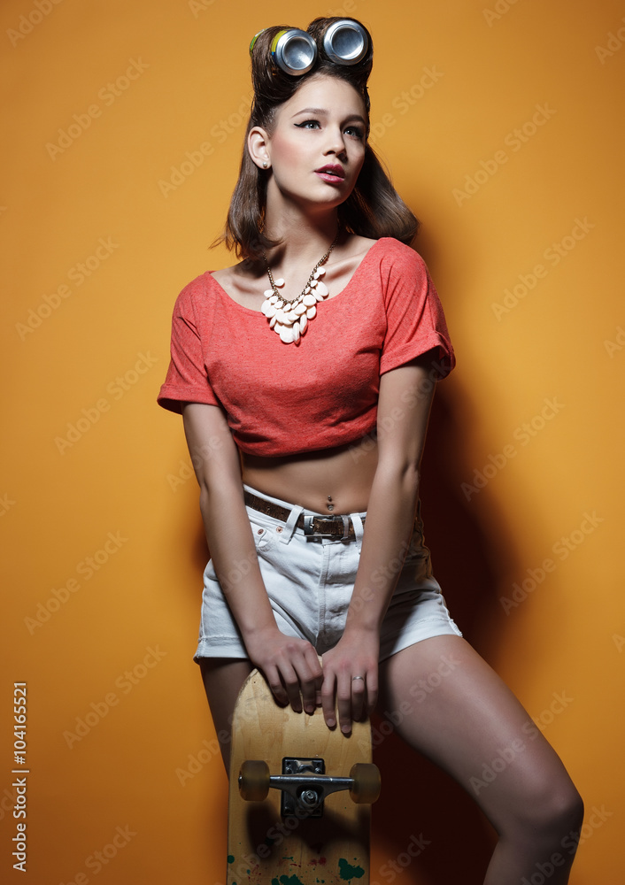 Beautiful fashionable girl with a skateboard in front of yellow background Beautiful fashionable girl with a skateboard in front of yellow background