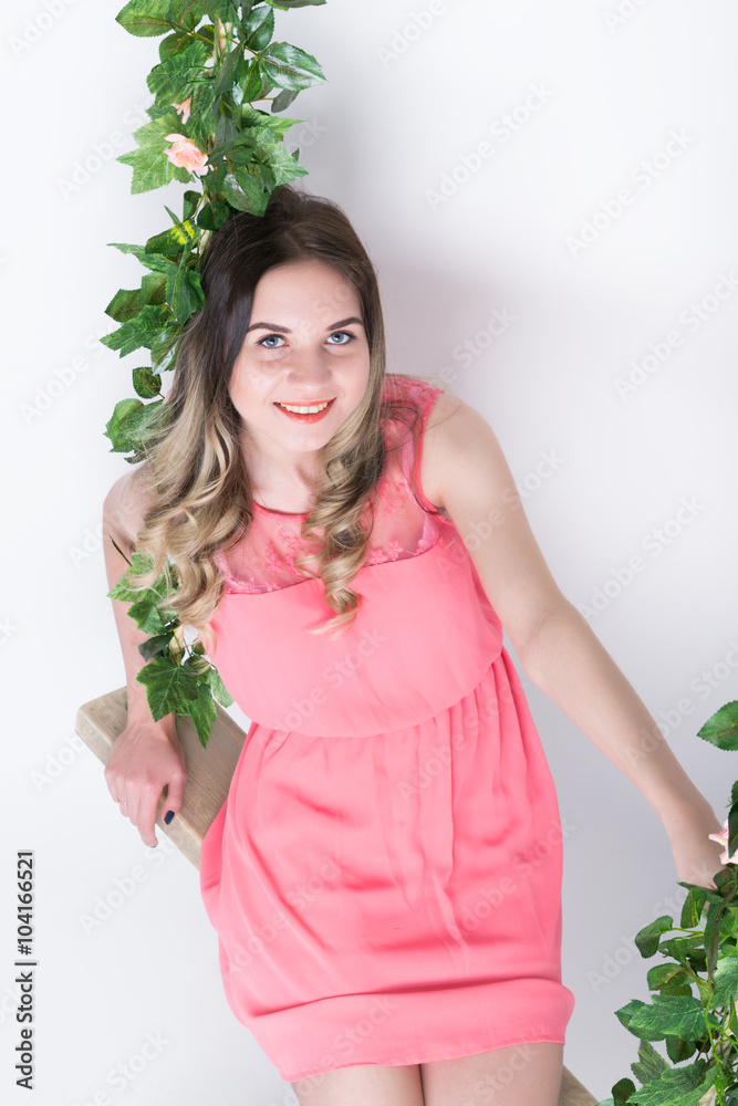 Beautiful young leggy blonde in a little pink dress and red high-heeled shoes on a swing, wooden swing suspended from a rope hemp, rope wrapped vine and ivy Beautiful young leggy blonde in a little pink dress and red high-heeled shoes on a swing, wooden swing suspended from a rope hemp, rope wrapped vine and ivy