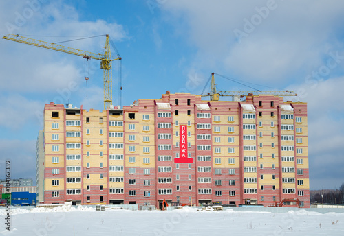 Construction cranes and housing under construction./ New modern apartment houses in the course of construction. On the house the poster with an inscription in Russian - sale.