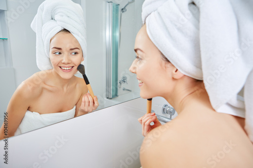 young woman applying face powder in the bathroom