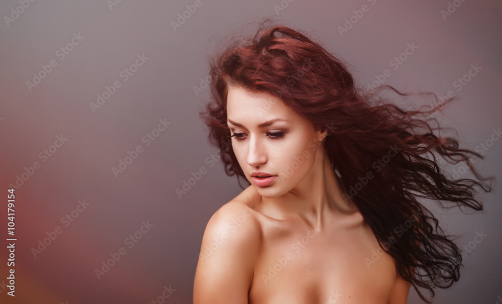 Naklejka premium Portrait of a beautiful young woman with curly hair on a gray background. Professional make-up and hairstyle. Fashion art photo