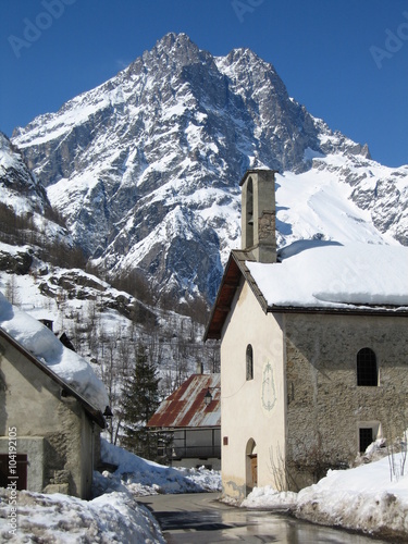 Snow covered mountain and traditional French village street in the Queyras region of the Southern French Hautes Alpes on a sunny day in early Spring 