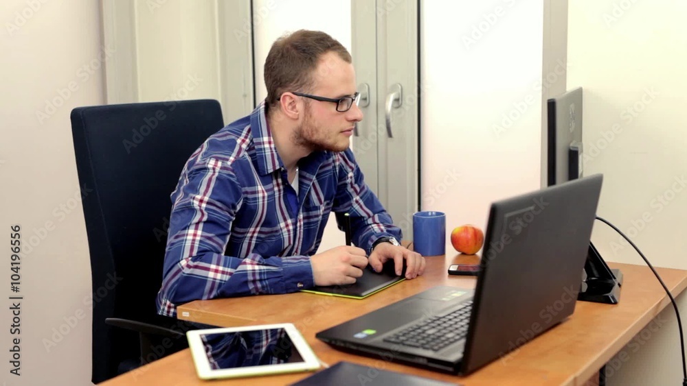 Handsome men sitting behind the desk and using two computers at the same time. He is focused on his work. Handsome men sitting behind the desk and using two computers at the same time. He is focused on his work.