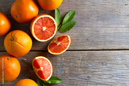 Fresh oranges with slices and leaves on wooden background.