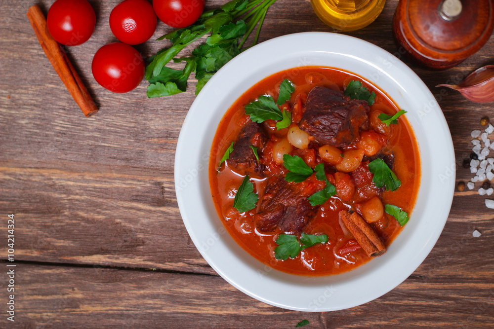 National Greek dish stifado with beef, tomatoes and onions, stewed in red wine with Herbs on a wooden background, horizontal National Greek dish stifado with beef, tomatoes and onions, stewed in red wine with Herbs on a wooden background, horizontal