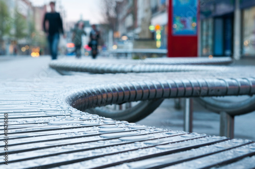 Street Seat.
Close up on a curvy, s-shaped seat, with raindrops. Out of focus pedestrians in the background. Taken in Exeter, Devon. photo