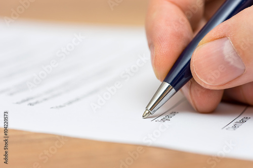 closeup of pen and human fingers signing document