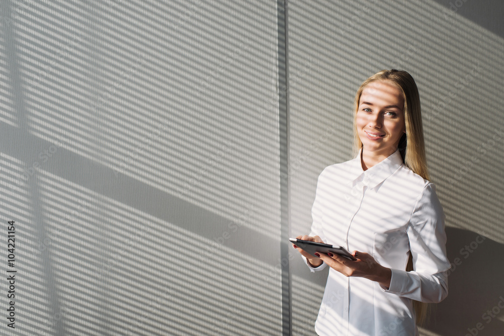 Young blonde businesswoman standing in office, holding tablet,, smiling looking at the camera. Young blonde businesswoman standing in office, holding tablet,, smiling looking at the camera.